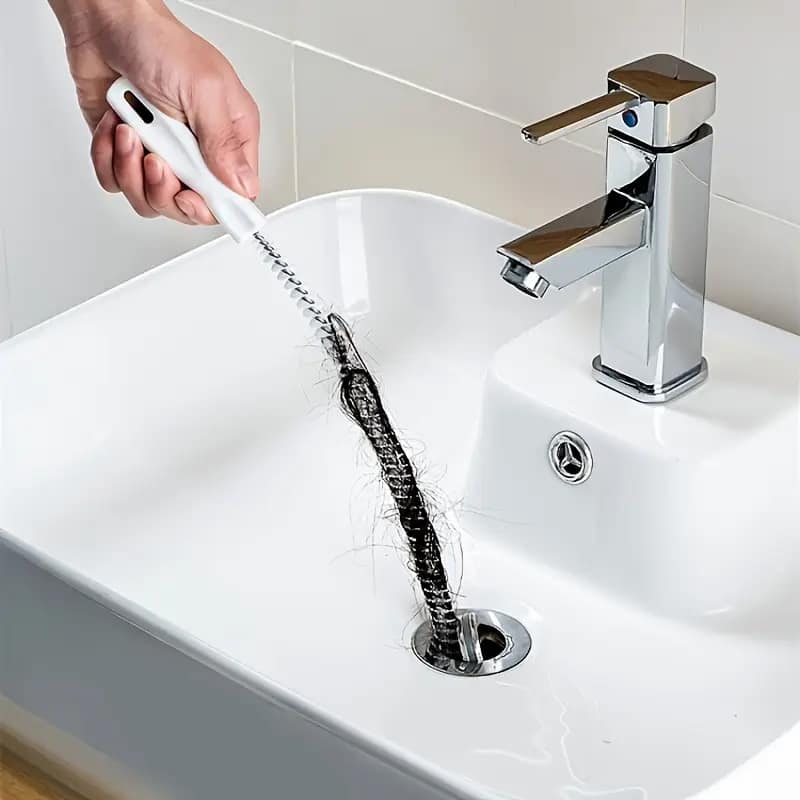 hand using flexible spiral drain cleaning brush to remove hair clog from bathroom sink drain to eliminate drain flies