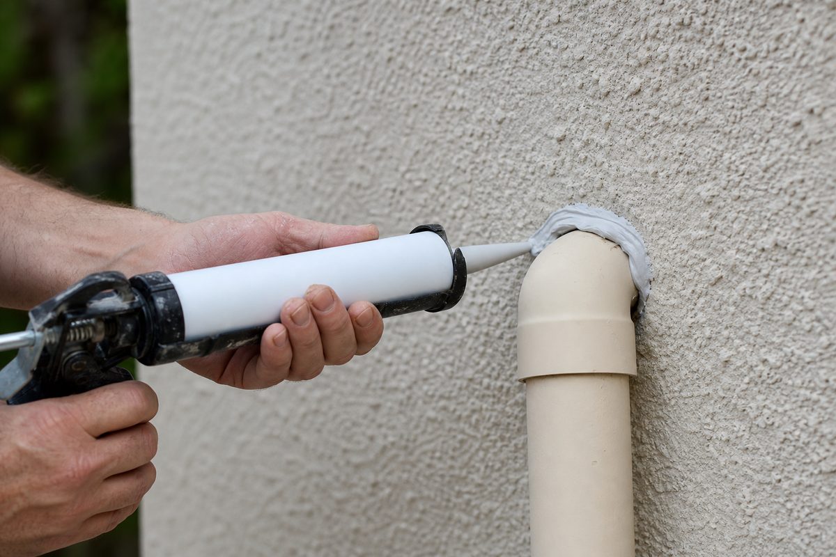 Applying caulk to seal a pipe gap in an exterior wall for scorpion prevention